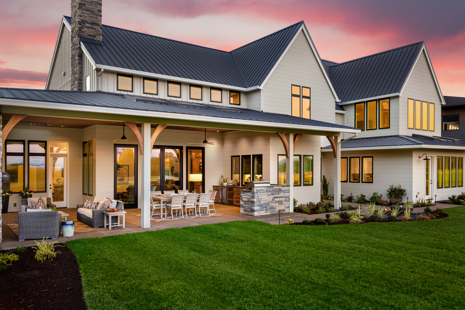 Beautiful luxury home exterior at sunset, featuring large covered patio with outdoor kitchen and barbecue